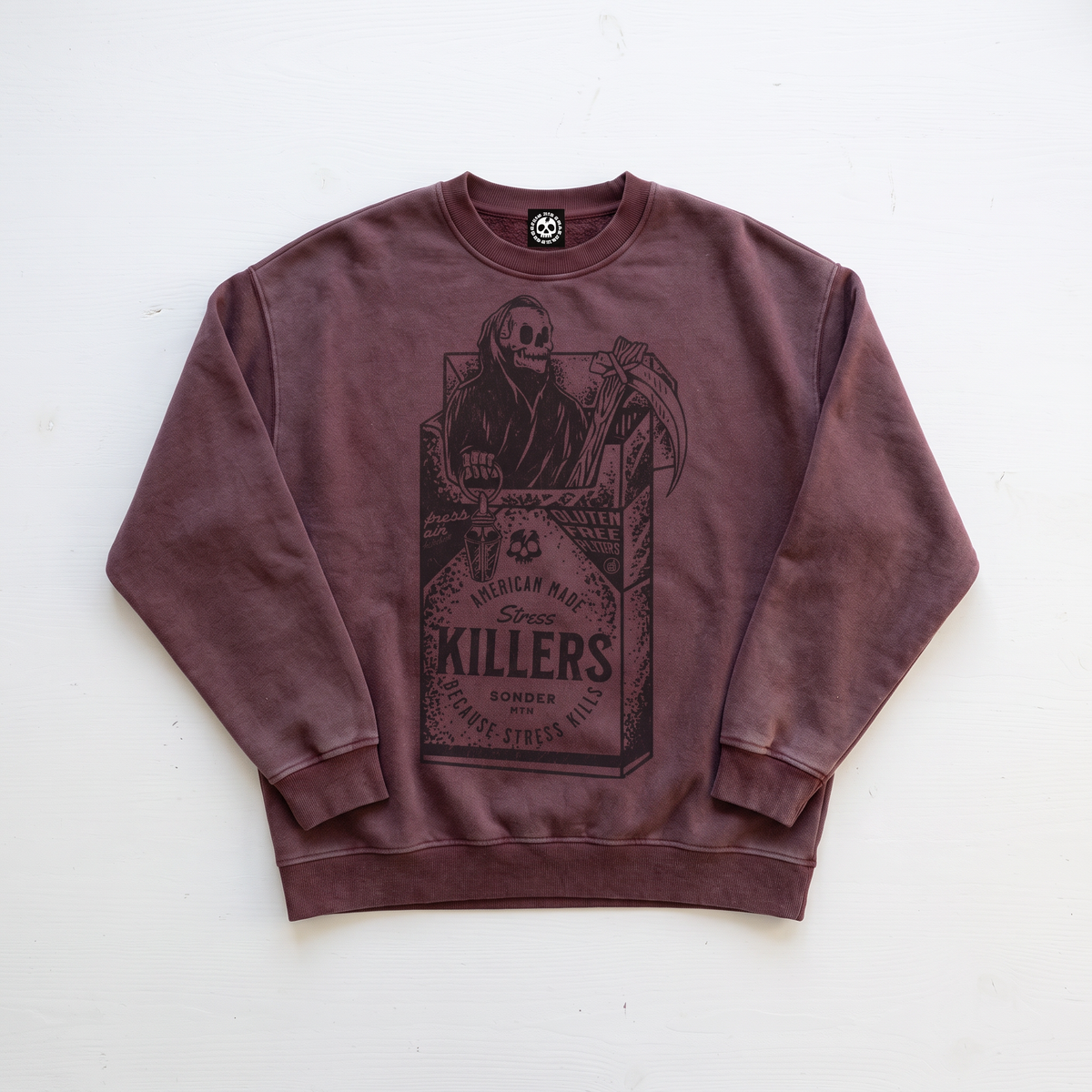 A washed dark brown crewneck sweatshirt featuring a large graphic print of a skeleton in a cigarette pack labeled 'KILLERS' on the front, laid flat on a white background.