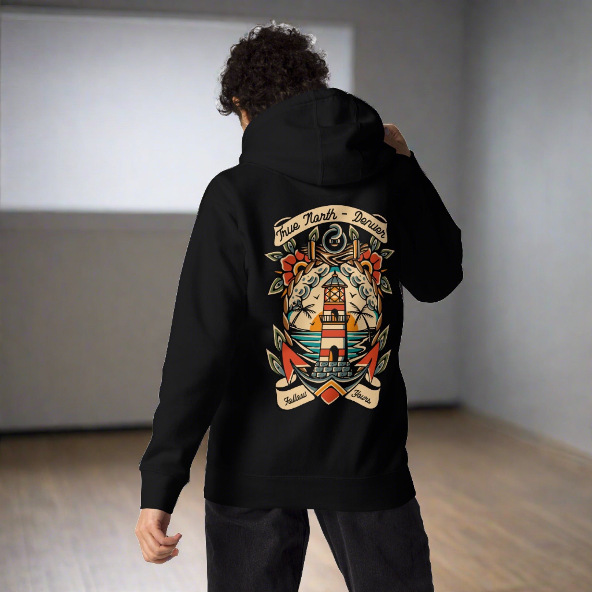A person wearing a black hoodie with a graphic print of a lighthouse, waves, and a seagull on the front.